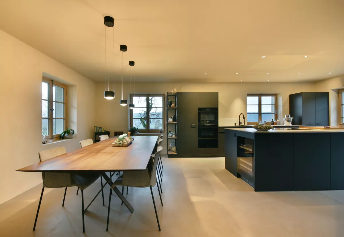 Essbereich mit moderner schwarzer Küche, drei hängenden runden Leuchten oberhalb vom Holzesstisch