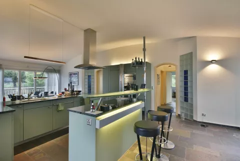 Moderne offene Küche in Metalfarbe mit Dunstabzugshauben an der Decke, LED-Spots in die Küchenwand integriert, Essbar mit Hockern, langgestreckte hängende Lampe über der Arbeitsfläche