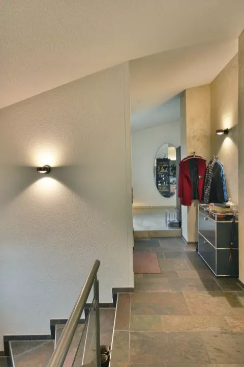 Zweiter Stock mit Steinboden, Treppe links hinunter, zwei runde Lampen an der Wand mit Licht, das nach oben und unten strahlt