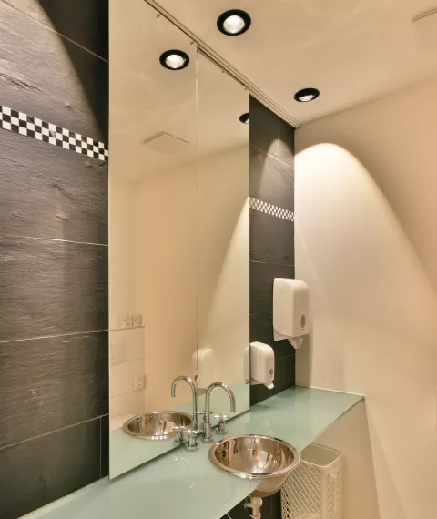 Modernes Badezimmer mit grossem Spiegel an einer schwarzen Steinwand, Deckenspots über dem Waschbecken
