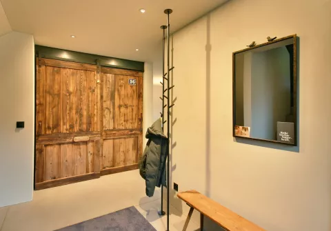 Eingangsbereich mit breiter Holztür, kleiderständer mit hängender Jacke, Spiegel an der Wand oberhalb einer kleinen Holzbank und LED-Spots in der Decke