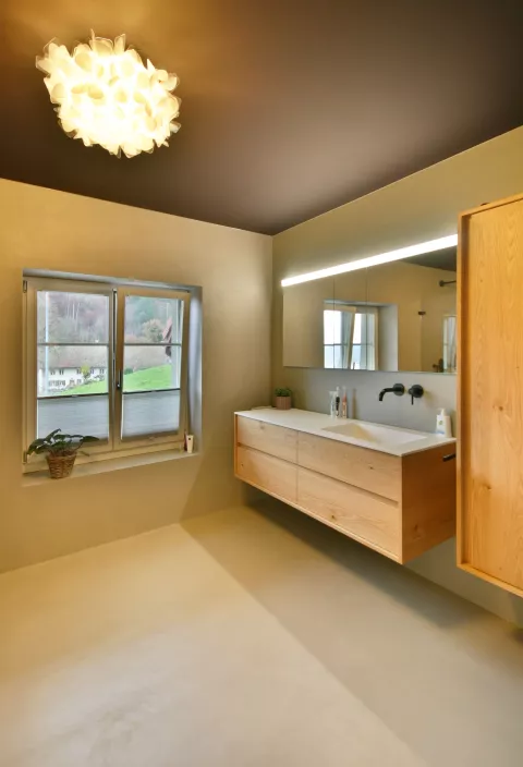 Modernes Badzimmer mit Holzmöbel, horizontaler Spiegel über der Spüle, mit LED-Linie darüber und runde wolkenähnliche Deckenlampe