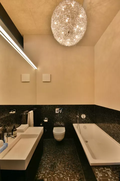 Modernes Badezimmer, helle Platten, elegante Deckenleuchte und dunklem Mosaik-Boden