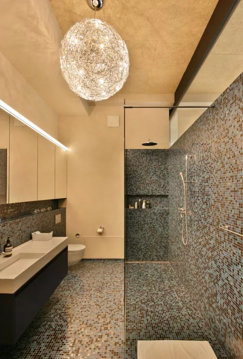 Badezimmer mit hellen Wänden, dunklem Mosaik-Boden und eleganter Deckenleuchte